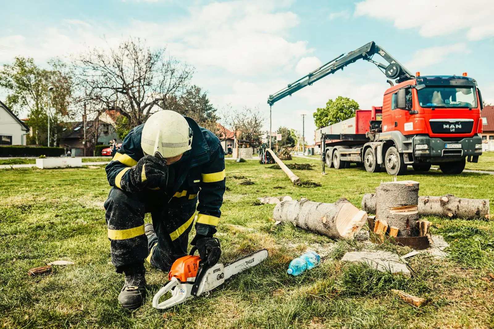 Tree service technician using a chainsaw beside a crane truck for hazardous removal work